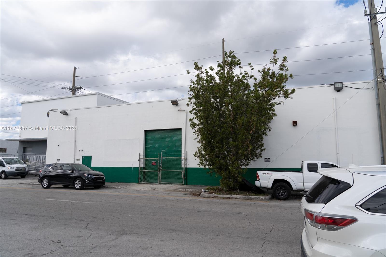 The exterior of a white and green industrial building features a roll-up door and trees — 1395 NW 22nd St, Miami FL 33142, MIAMI, FL