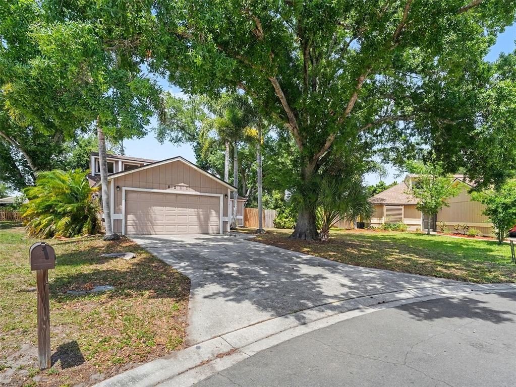 A tan house with a two-car garage and a large tree in the front yard — 8211 COUNTRY OAKS COURT, SARASOTA, FL