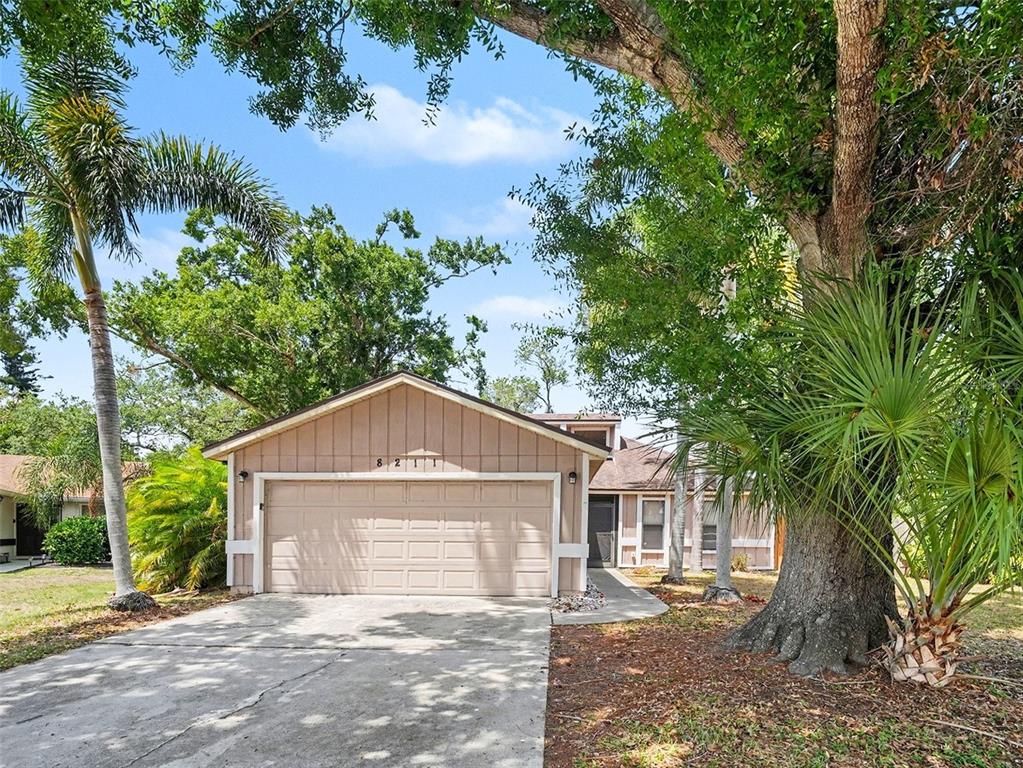 A single-story house with a beige garage and siding sits behind a large oak tree — 8211 COUNTRY OAKS COURT, SARASOTA, FL