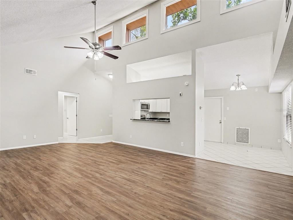 A spacious living room with vaulted ceilings, wood-look flooring, and an open kitchen pass-through window — 8211 COUNTRY OAKS COURT, SARASOTA, FL