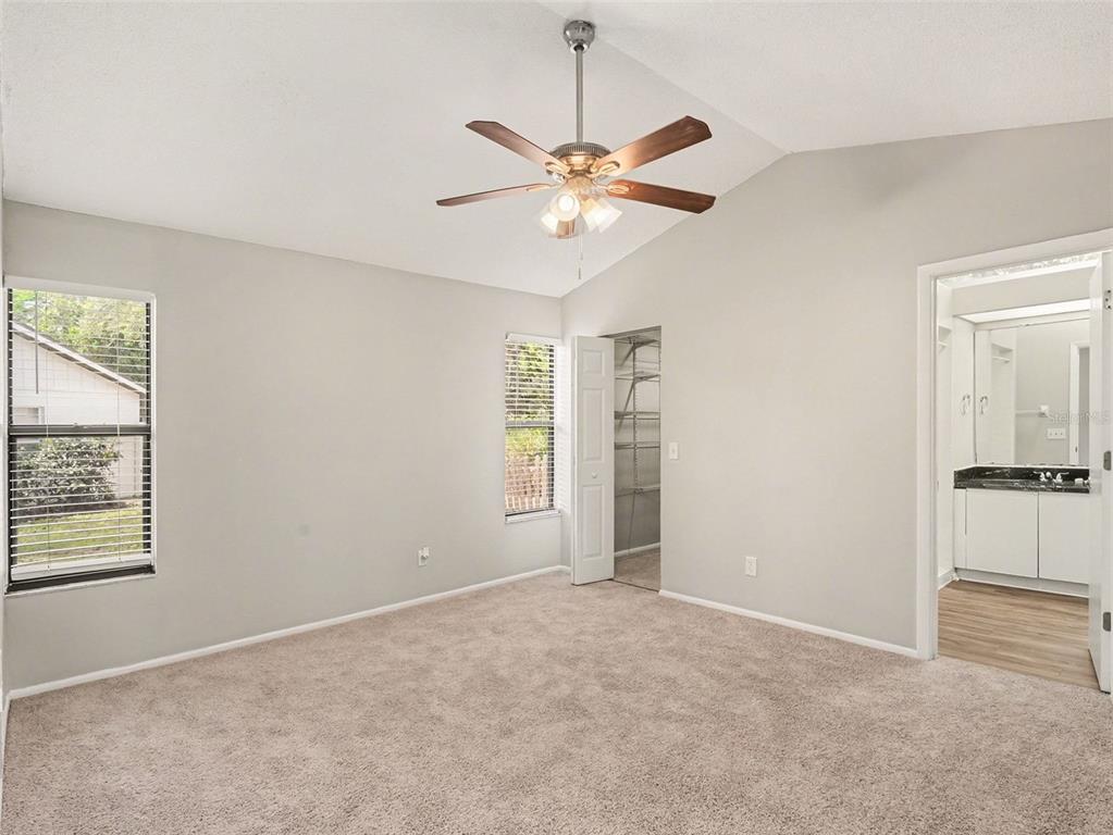 A bedroom with beige carpet, light gray walls, a ceiling fan, and an attached bathroom — 8211 COUNTRY OAKS COURT, SARASOTA, FL