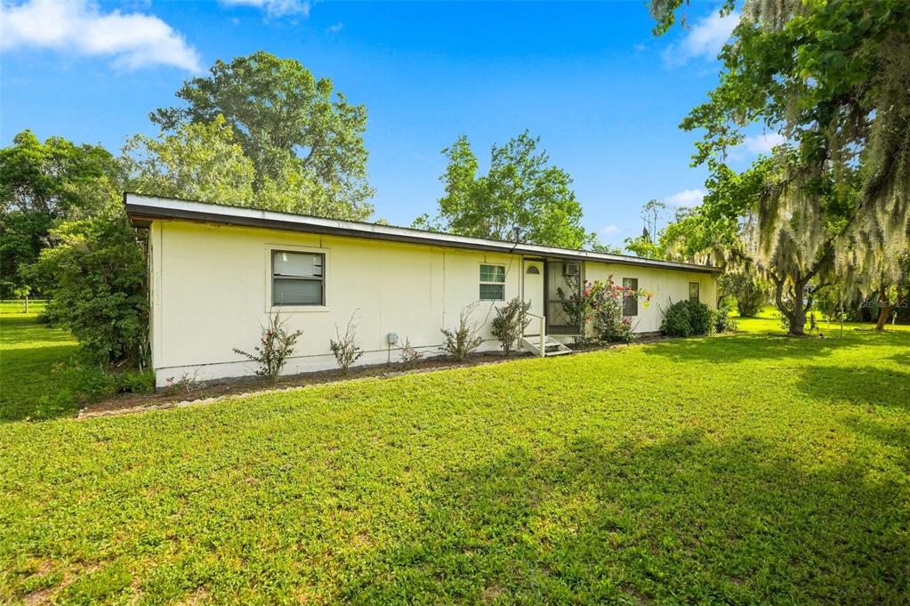 A single-story house with light yellow siding sits on a grassy lawn under blue skies — 13637 CR 737, WEBSTER, FL
