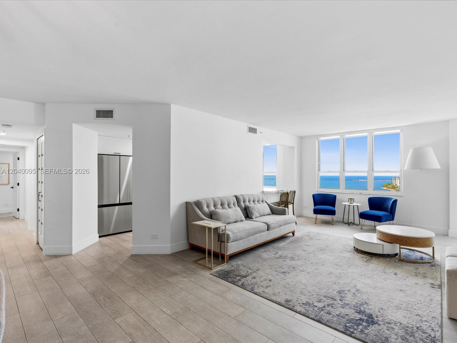 A living room with light wood floors, a grey sofa, blue chairs, and ocean views — 701 Brickell Key Blvd # 1903, Miami FL 33131, MIAMI, FL