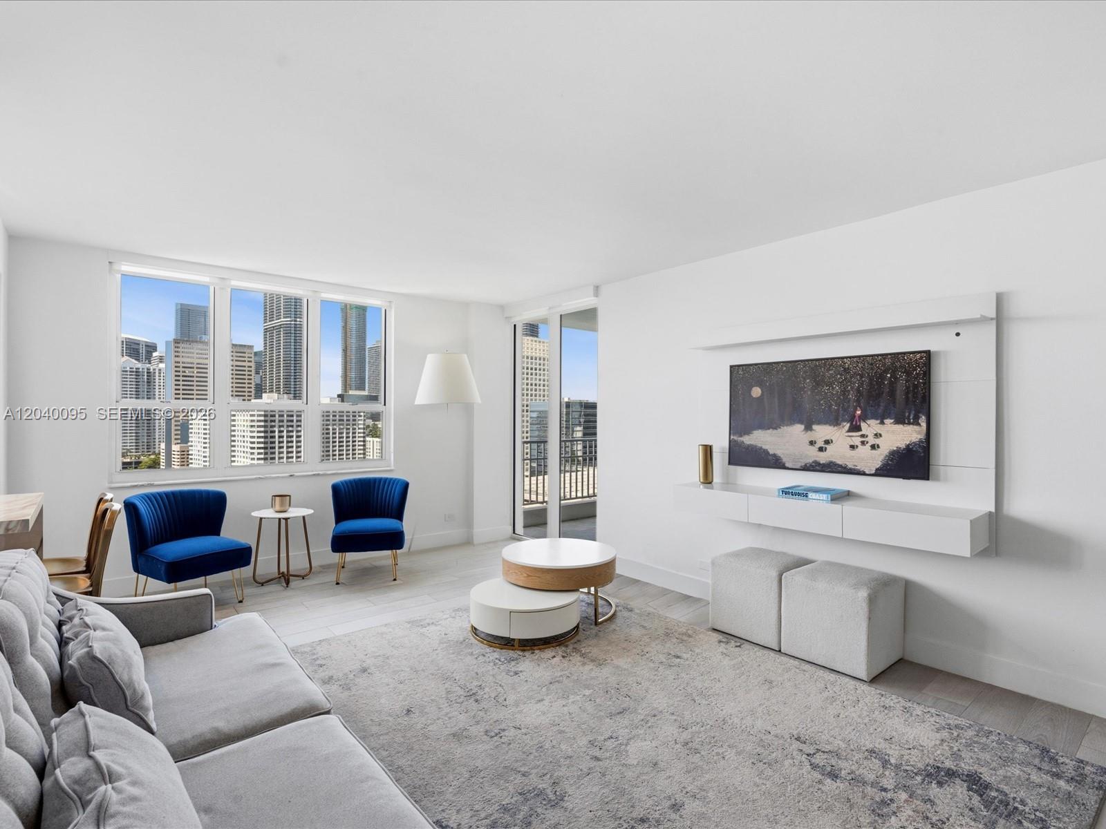 A bright living room features a gray sofa, blue accent chairs, and a city view — 701 Brickell Key Blvd # 1903, Miami FL 33131, MIAMI, FL