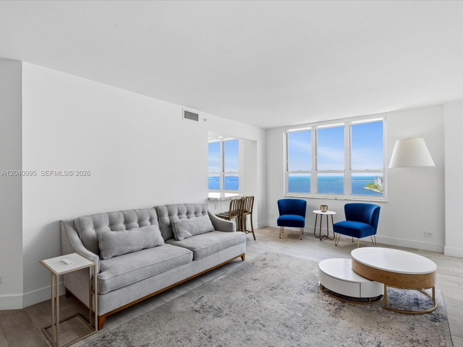 A living room features a grey tufted sofa, two blue chairs, and ocean views — 701 Brickell Key Blvd # 1903, Miami FL 33131, MIAMI, FL