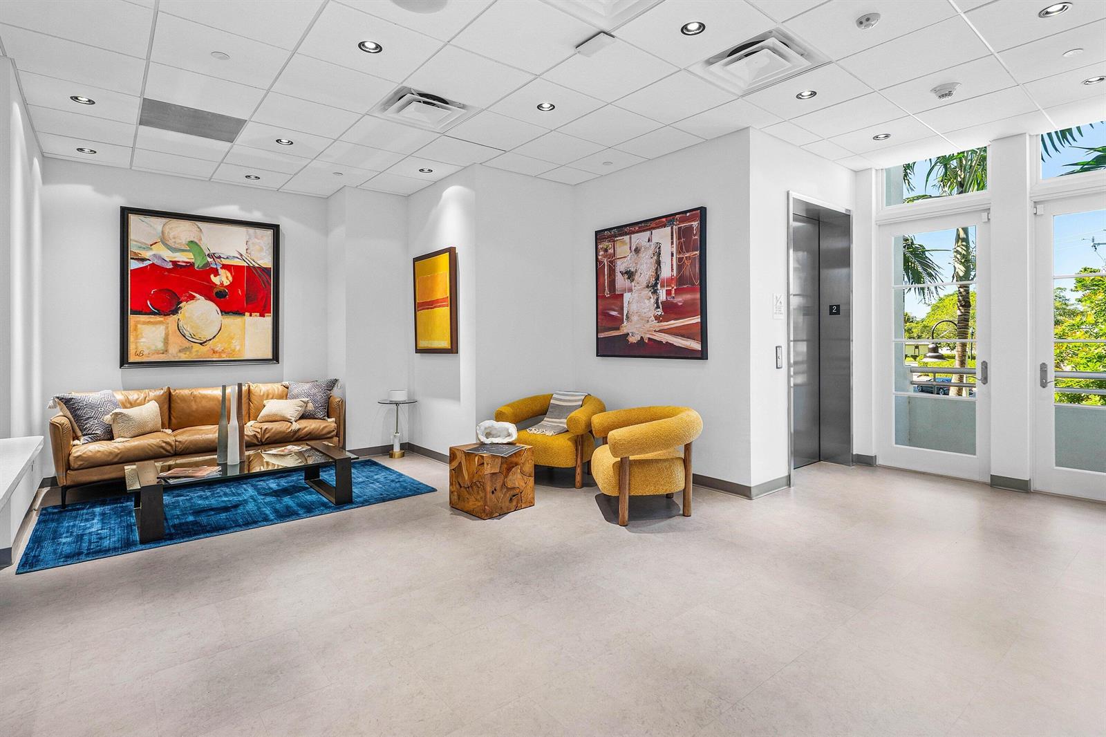 A modern lobby features a leather sofa, two yellow armchairs, abstract art, and an elevator — 226 Palm Court, Delray Beach FL 33444, DELRAY BEACH, FL