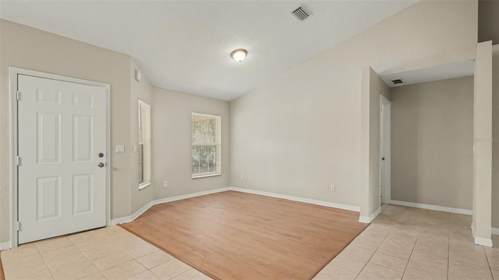 An empty room features light wood-look flooring, beige walls, and a white entry door — 5427 SW 87TH PLACE, OCALA, FL