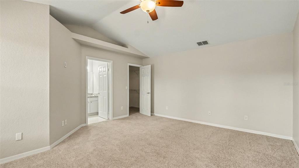 A carpeted bedroom features a vaulted ceiling, a ceiling fan, and two open doorways — 5427 SW 87TH PLACE, OCALA, FL