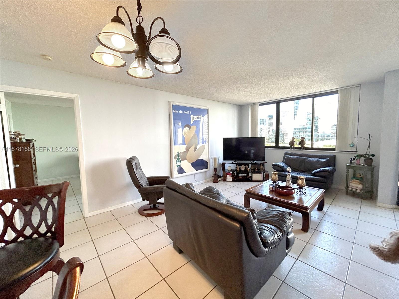A living room features tile flooring, leather furniture, a chandelier, and a large window view — 540 Brickell Key Dr # 811, Miami FL 33131, MIAMI, FL