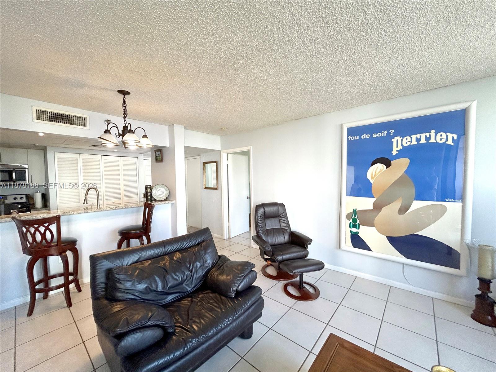 A living room with a black leather sofa, recliner, and a large Perrier wall poster — 540 Brickell Key Dr # 811, Miami FL 33131, MIAMI, FL