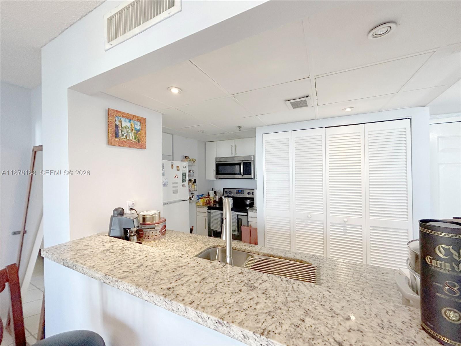 A kitchen features a granite countertop island with a sink and white louvered closet doors — 540 Brickell Key Dr # 811, Miami FL 33131, MIAMI, FL