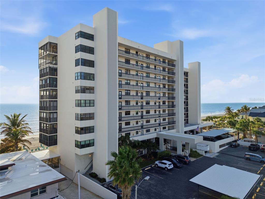 An exterior view of a multi-story beachfront condominium building with parking and palm trees — 15462 GULF BOULEVARD UNIT 406, MADEIRA BEACH, FL