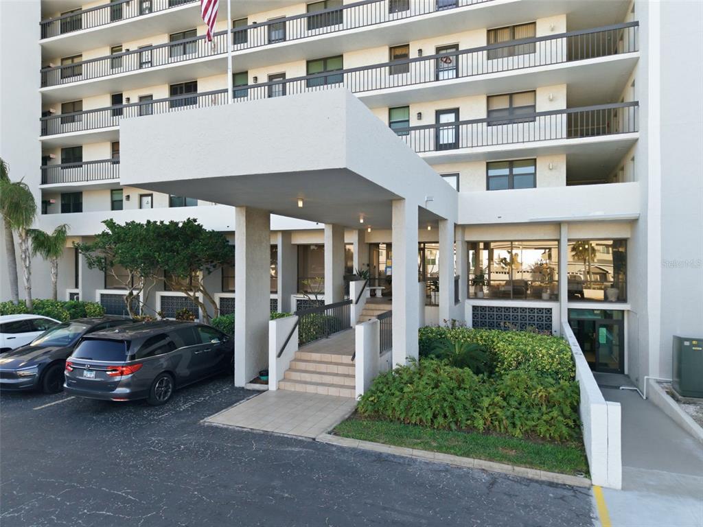 The exterior of a multi-story apartment building features a covered entrance with concrete stairs — 15462 GULF BOULEVARD UNIT 406, MADEIRA BEACH, FL