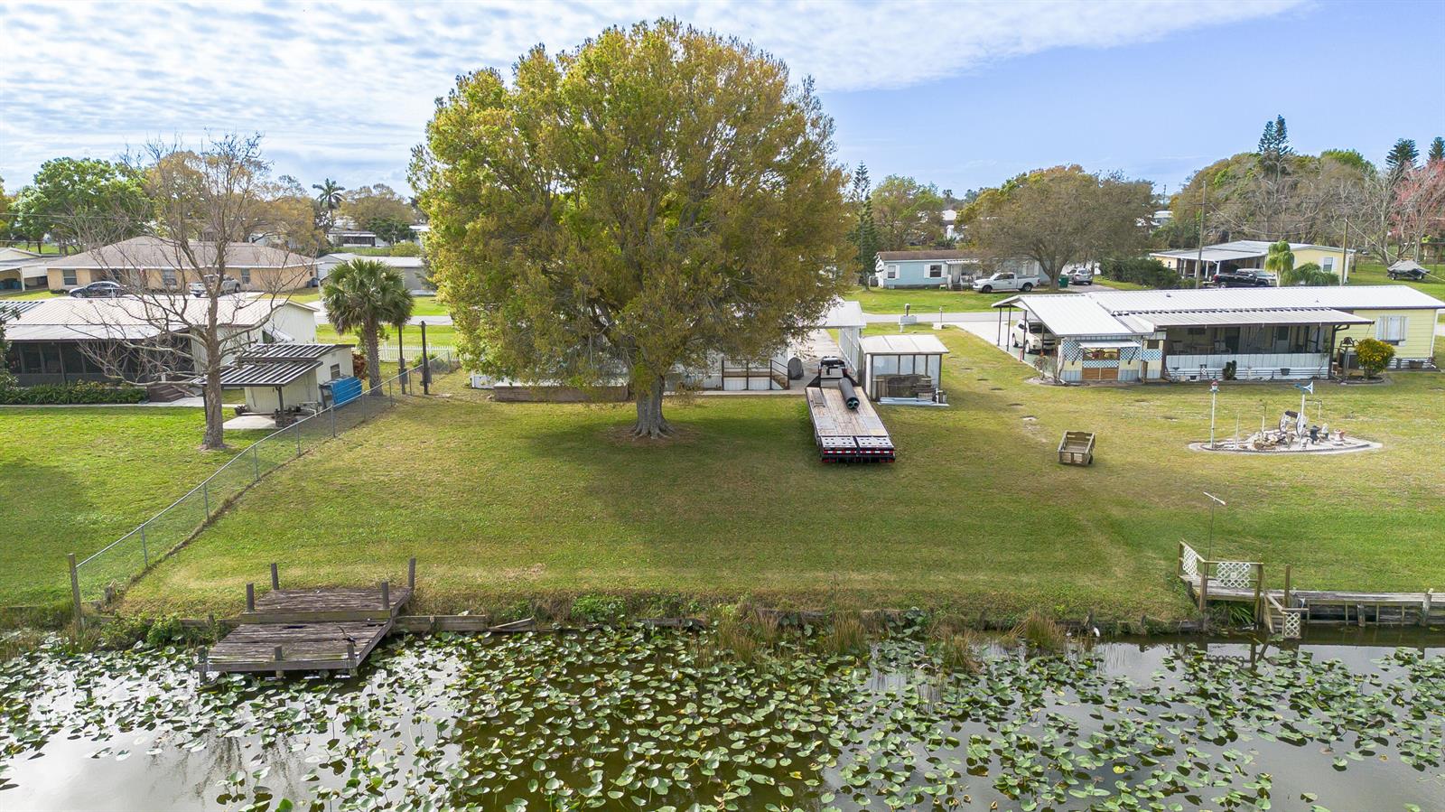 An aerial view shows a grassy backyard with a large tree, a trailer, and a dock — 2027 SE 27th Street, Okeechobee FL 34974, OKEECHOBEE, FL