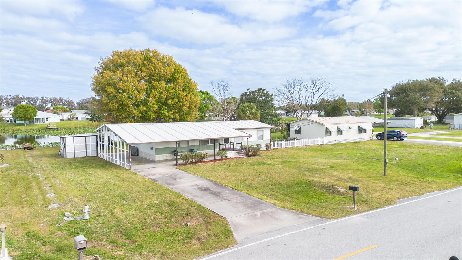 An aerial view shows a single-story house with a large carport and a nearby pond — 2027 SE 27th Street, Okeechobee FL 34974, OKEECHOBEE, FL