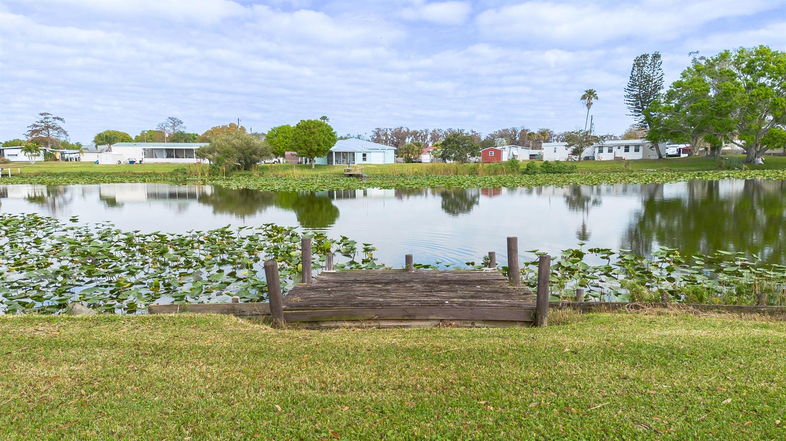 A wooden dock extends into a pond covered with lily pads in a residential neighborhood — 2027 SE 27th Street, Okeechobee FL 34974, OKEECHOBEE, FL
