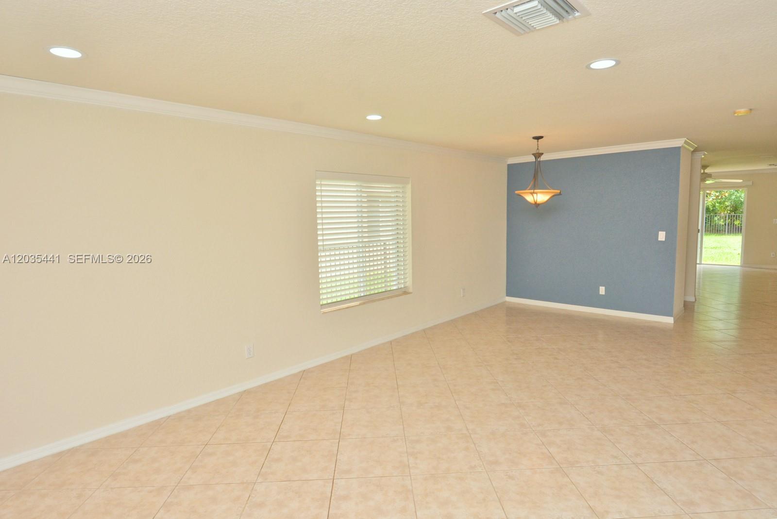 A spacious room features beige tile flooring, a blue accent wall, and a hanging light — 4648 56th Ln, Vero Beach FL 32967, VERO BEACH, FL