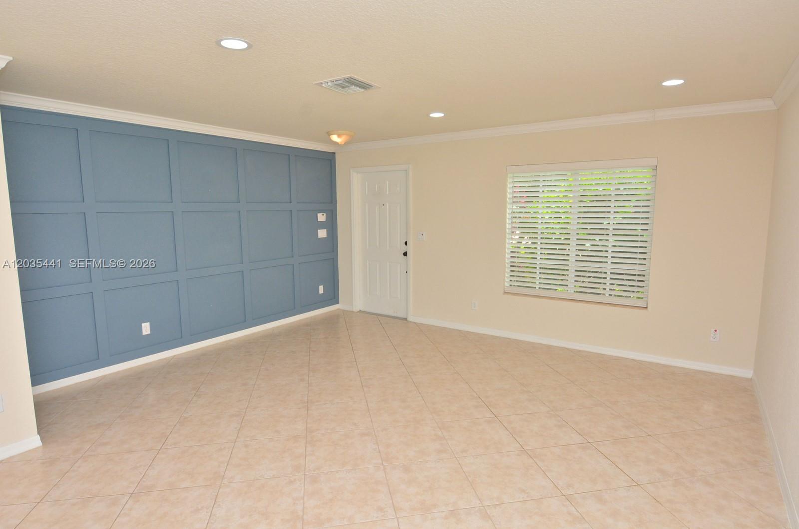An empty room features beige tile flooring, a blue paneled accent wall, and a window — 4648 56th Ln, Vero Beach FL 32967, VERO BEACH, FL