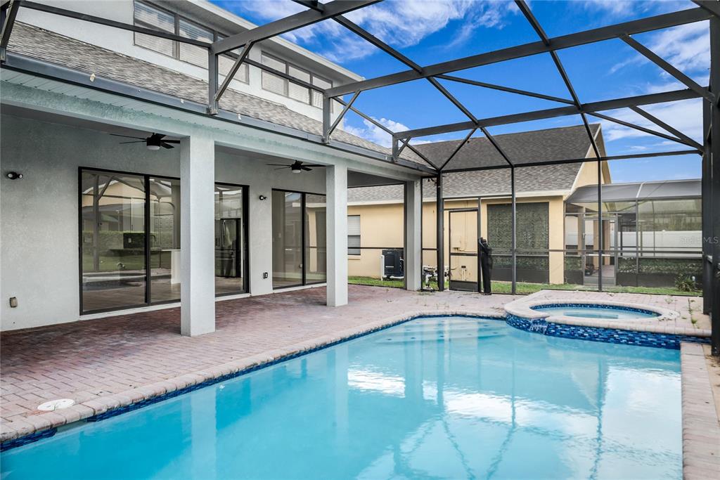 A swimming pool and spa are enclosed within a screened lanai behind a house — 563 LAKE DAVENPORT CIRCLE, DAVENPORT, FL