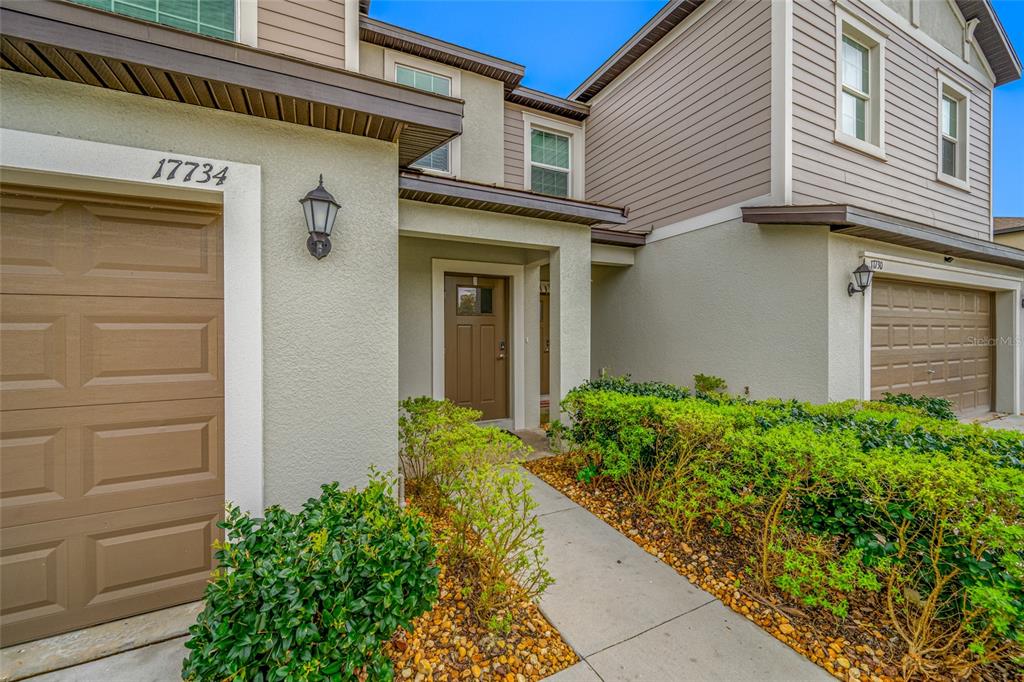 The exterior of a two-story townhouse features a tan garage, a front door, and landscaping — 17734 NECTAR FLUME DRIVE, LAND O LAKES, FL