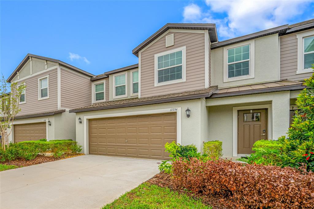 A two-story townhouse with a tan garage, brown front door, and light-colored siding — 17734 NECTAR FLUME DRIVE, LAND O LAKES, FL