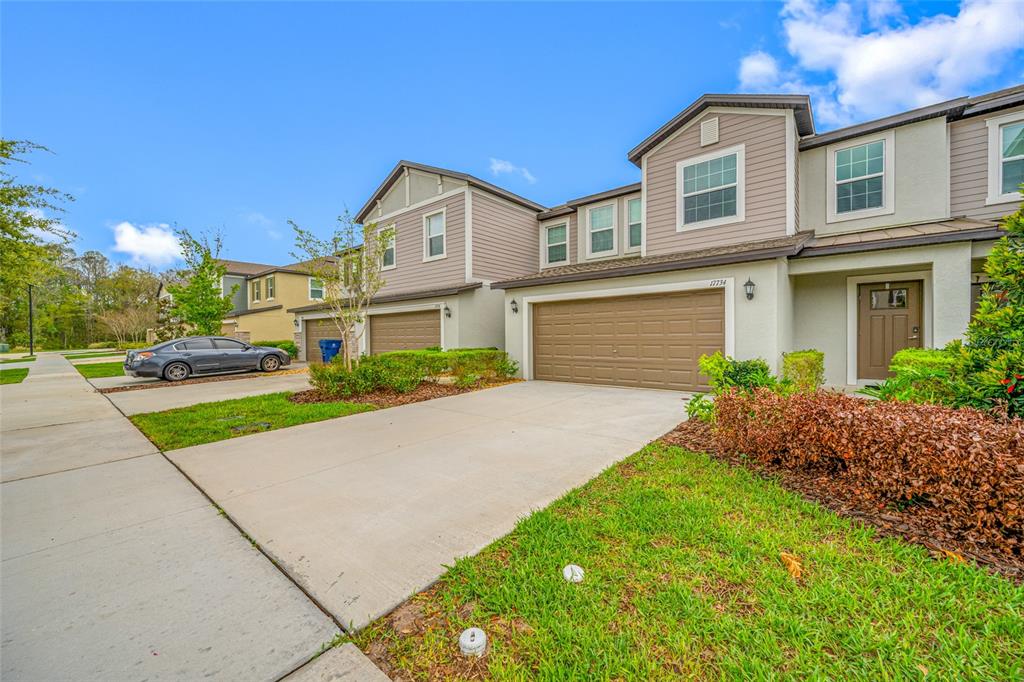 A multi-story townhouse exterior features a beige facade, a brown garage door, and a driveway — 17734 NECTAR FLUME DRIVE, LAND O LAKES, FL