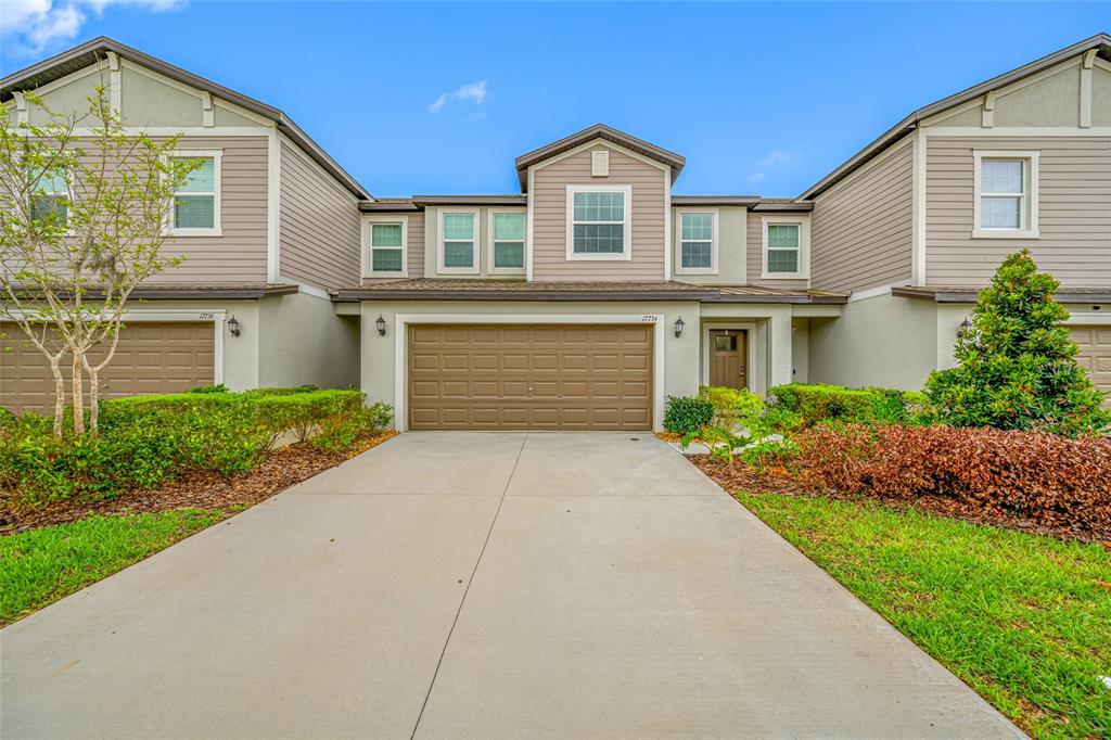 A two-story townhouse with a brown garage door, beige siding, and a concrete driveway — 17734 NECTAR FLUME DRIVE, LAND O LAKES, FL