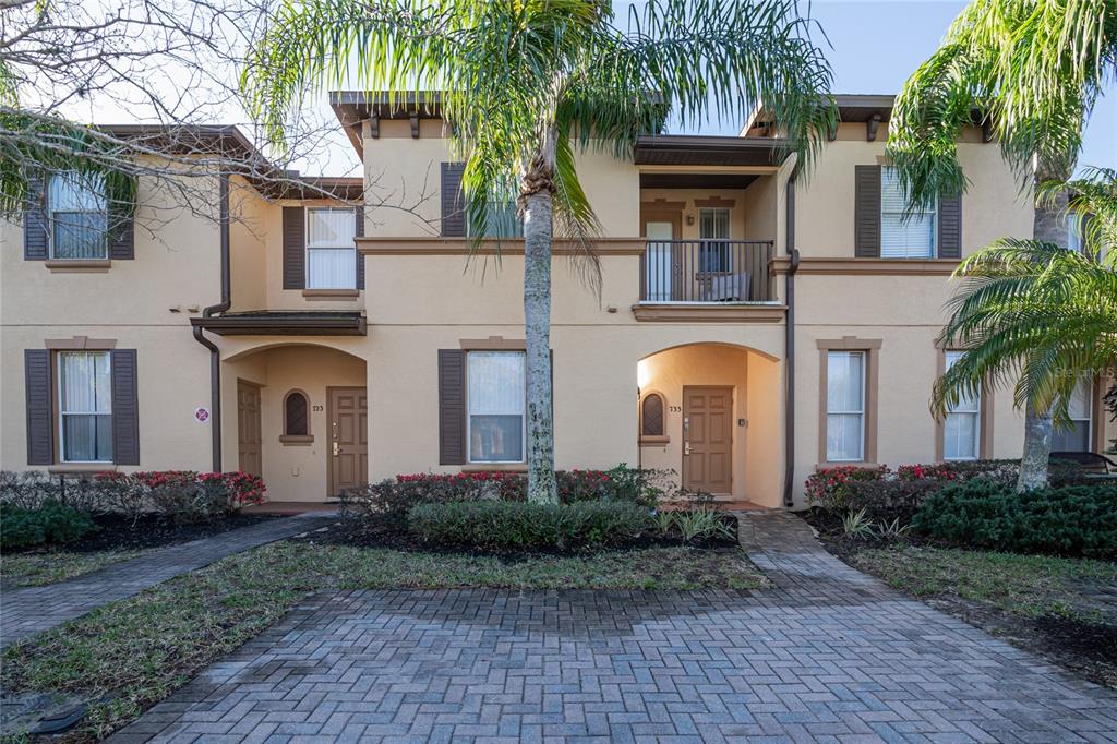 A two-story tan stucco townhouse features a brick paver driveway and palm trees — 733 CALABRIA AVENUE, DAVENPORT, FL