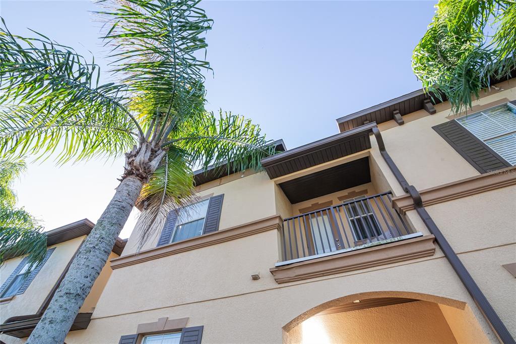 A low-angle view of a tan stucco building exterior with a balcony and palm trees — 733 CALABRIA AVENUE, DAVENPORT, FL