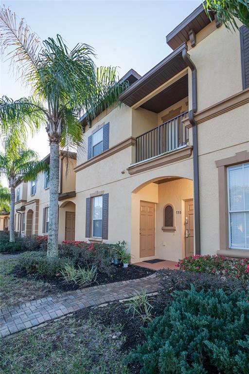 Exterior view of a two-story tan townhouse with a balcony and a brick walkway — 733 CALABRIA AVENUE, DAVENPORT, FL
