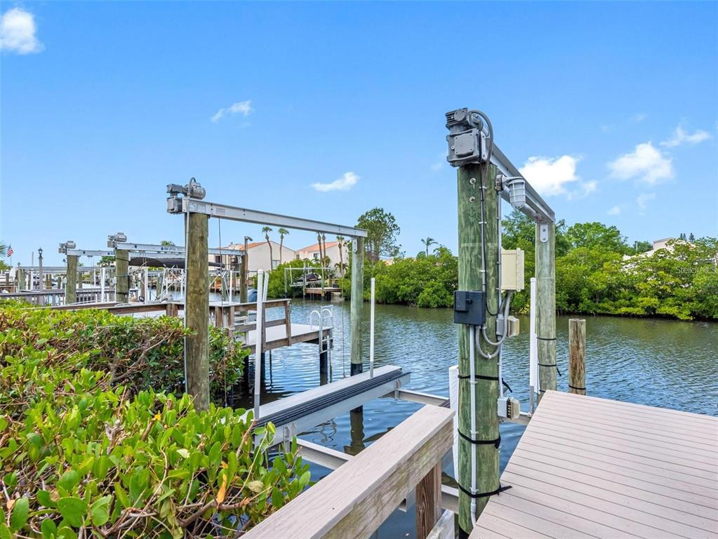 A wooden dock features a boat lift with metal framing over a calm canal — 4306 SUNRAY COURT, TAMPA, FL