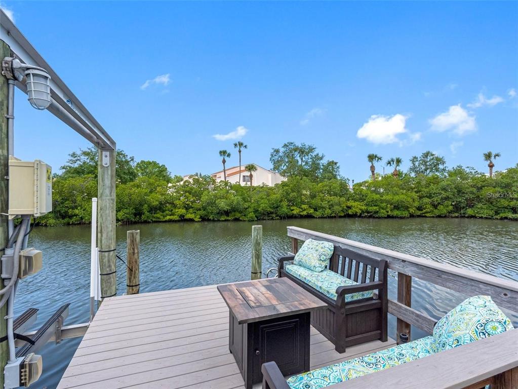 A wooden dock features a fire pit table and bench seating overlooking a canal — 4306 SUNRAY COURT, TAMPA, FL