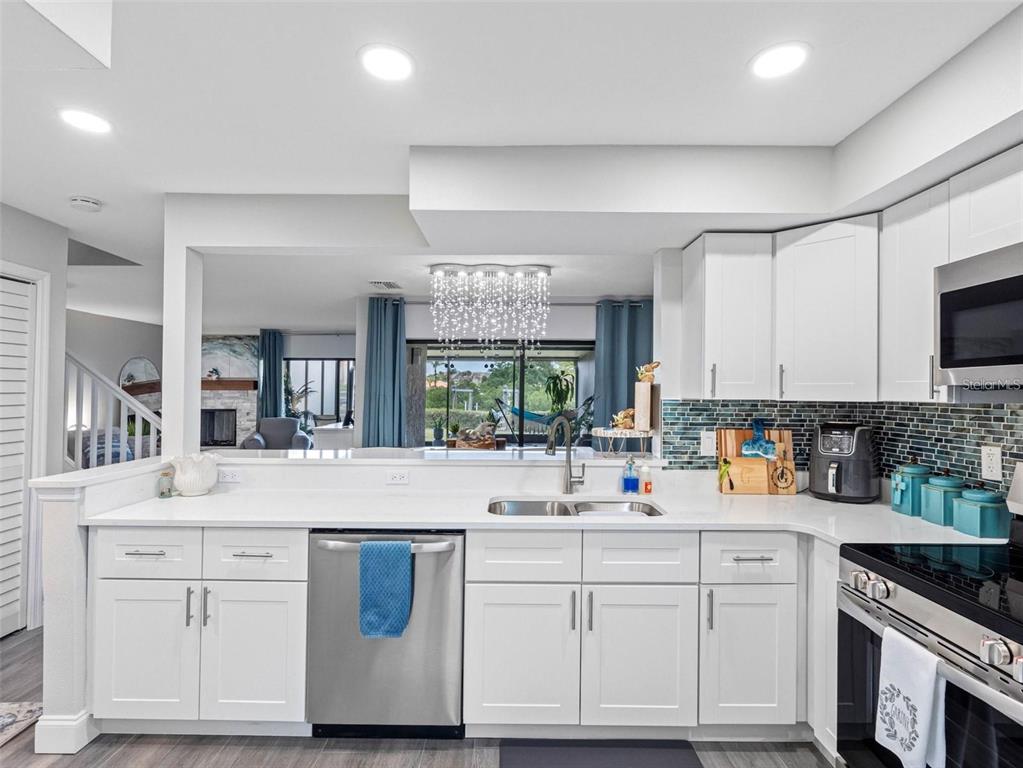 A white kitchen with stainless steel appliances, quartz countertops, and a view into the living room — 4306 SUNRAY COURT, TAMPA, FL