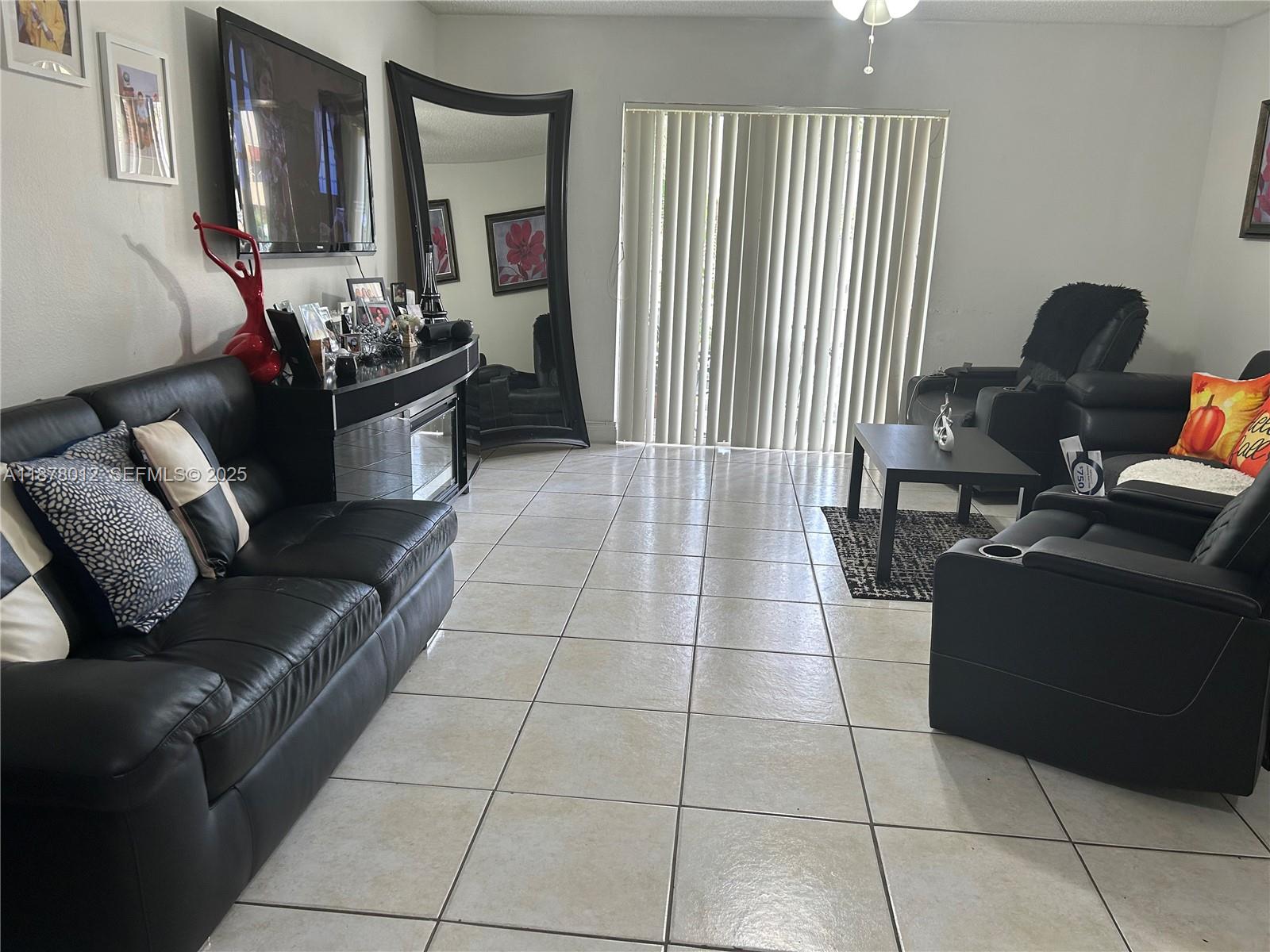 A living room features black leather furniture, a large floor mirror, and light tile flooring — 17901 NW 68th Ave # T101, Hialeah FL 33015, HIALEAH, FL