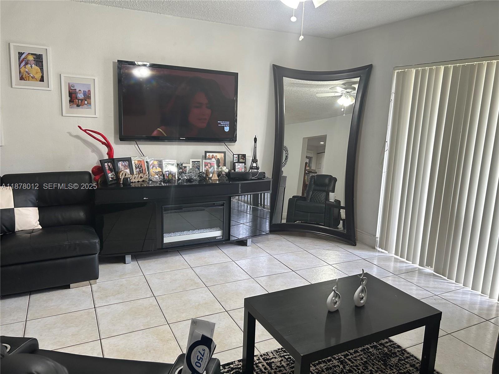 A living room features a black media console with a fireplace, a large mirror, and tile flooring — 17901 NW 68th Ave # T101, Hialeah FL 33015, HIALEAH, FL