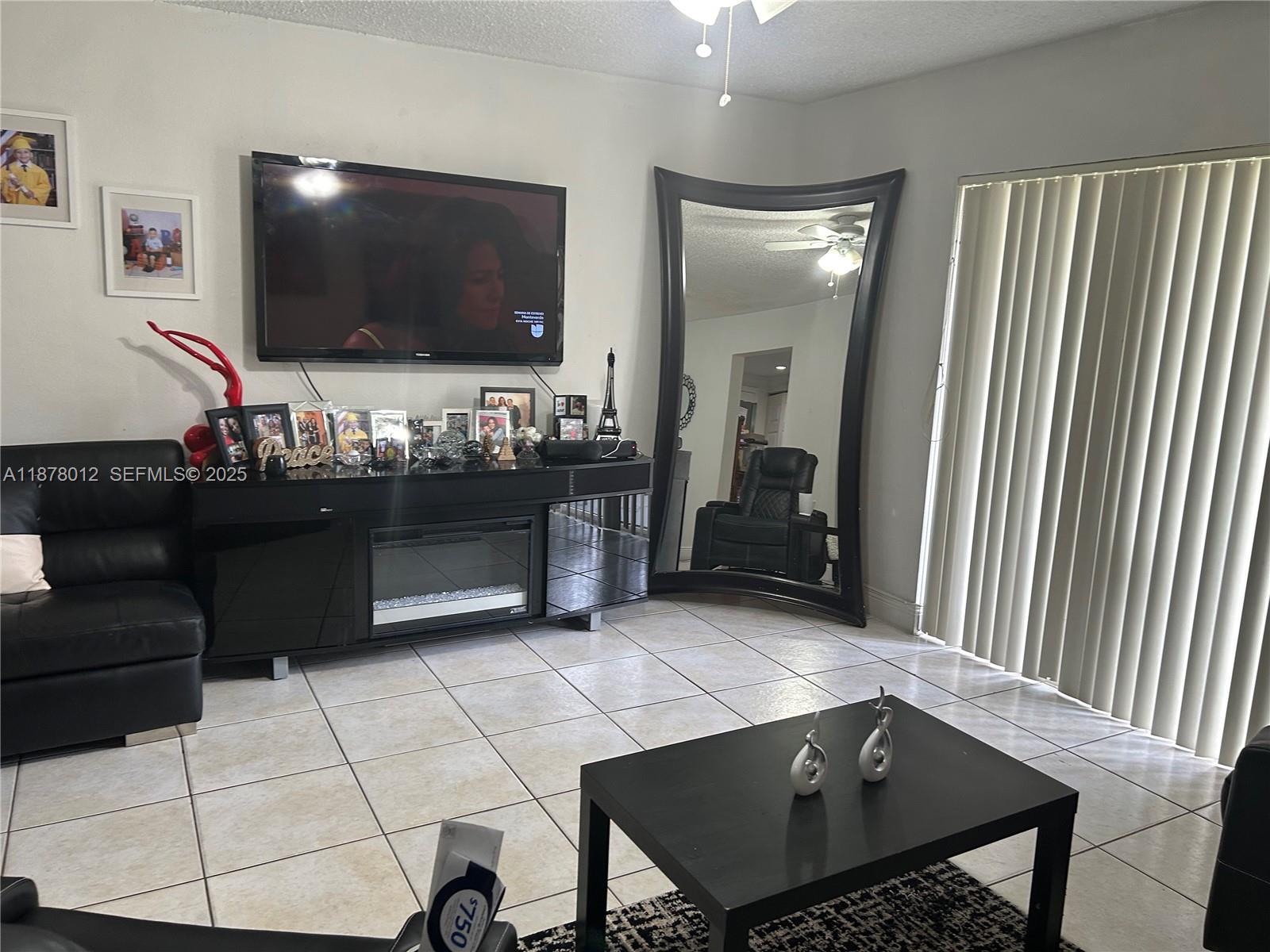 A living room features a black entertainment console with a fireplace, television, and large mirror — 17901 NW 68th Ave # T101, Hialeah FL 33015, HIALEAH, FL
