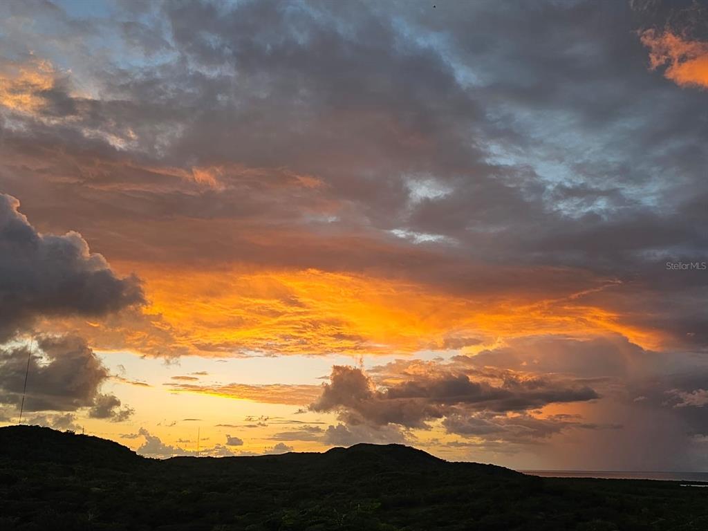 A vibrant sunset illuminates a cloudy sky above a dark, hilly landscape — Carr 301 km 3.2 MONTELCARLO STATE, CABO ROJO, PR