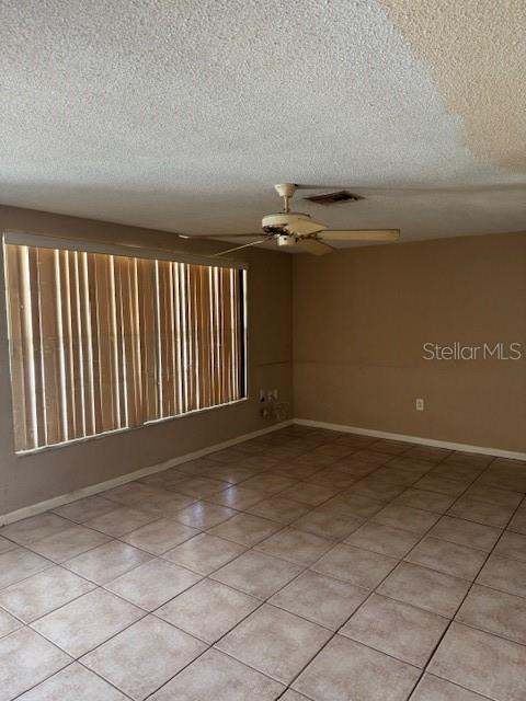 An empty room features beige tile flooring, a ceiling fan, and vertical window blinds — 8811 GOSHEN LANE, PORT RICHEY, FL