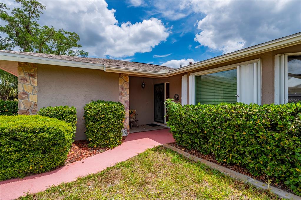 The exterior of a house features a stone-accented entryway, a pink walkway, and green hedges — 22317 LAIKA AVENUE, PORT CHARLOTTE, FL