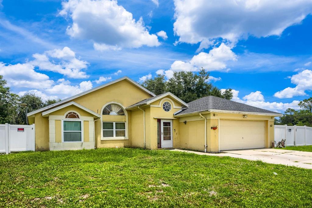 A yellow single-story house with a two-car garage and a white vinyl fence — 102 CARLISLE COURT, KISSIMMEE, FL