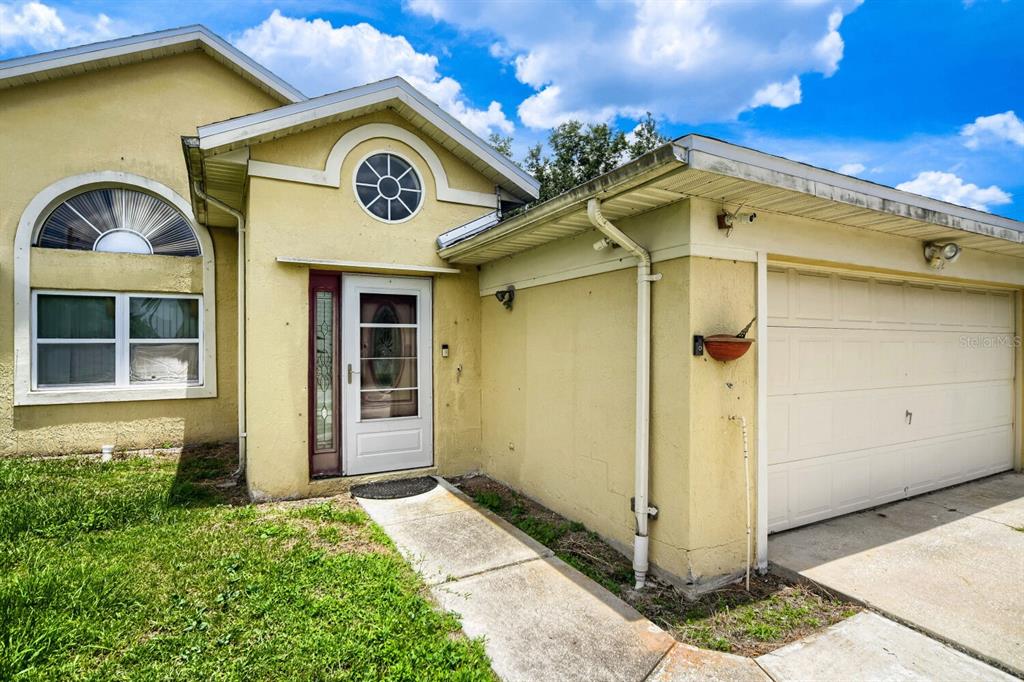 A yellow house exterior features a front door, a garage, and a large arched window — 102 CARLISLE COURT, KISSIMMEE, FL