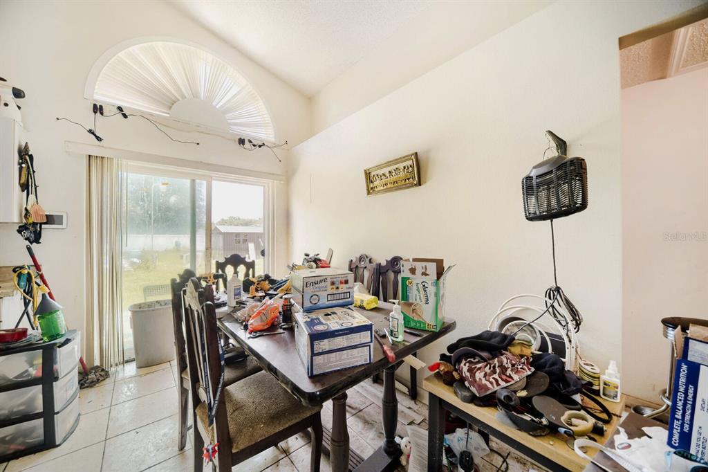 A cluttered dining area features a wooden table, tile flooring, and a large arched window — 102 CARLISLE COURT, KISSIMMEE, FL