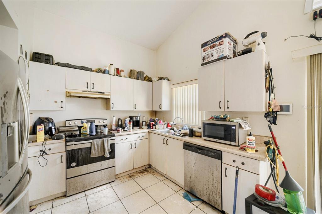 A kitchen with white cabinets, stainless steel appliances, and tiled floors in need of cleaning — 102 CARLISLE COURT, KISSIMMEE, FL