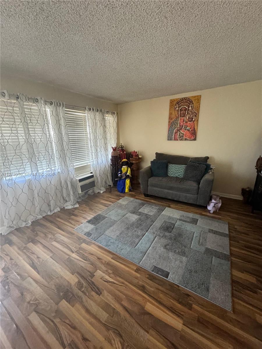 A living room features wood-look flooring, a gray loveseat, a patterned area rug, and curtains — 142 Northampton G # 142, West Palm Beach FL 33417, WEST PALM BEACH, FL