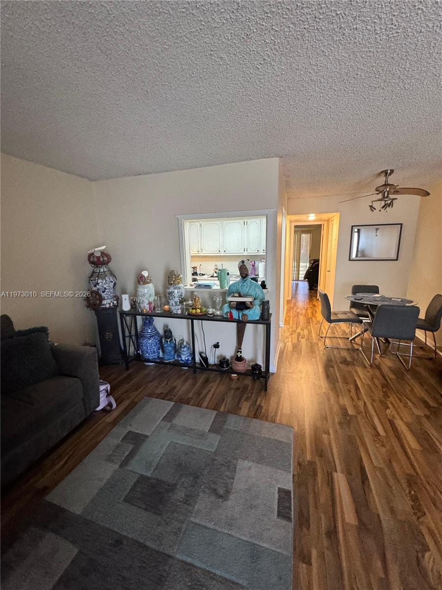 A living room features wood-look flooring, a pass-through window to the kitchen, and dining area — 142 Northampton G # 142, West Palm Beach FL 33417, WEST PALM BEACH, FL