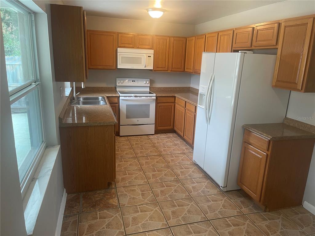 A kitchen features wood cabinets, white appliances, laminate countertops, and tiled flooring — 906 ESSEX ROAD, BRANDON, FL