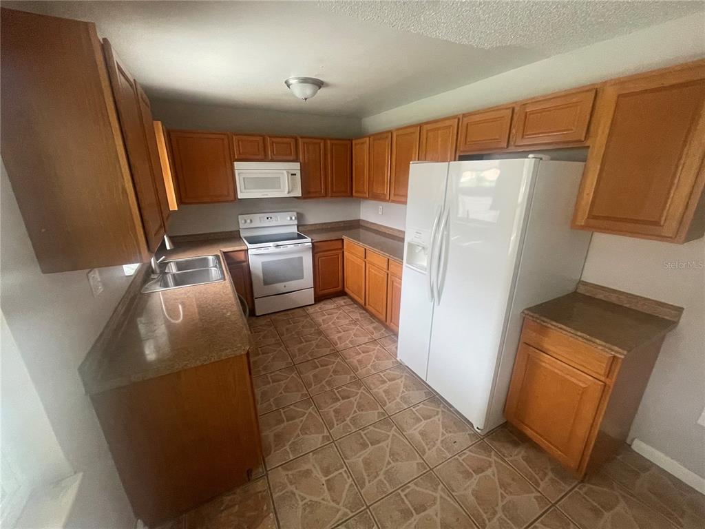 A kitchen features wood cabinets, white appliances, brown countertops, and tiled flooring — 906 ESSEX ROAD, BRANDON, FL