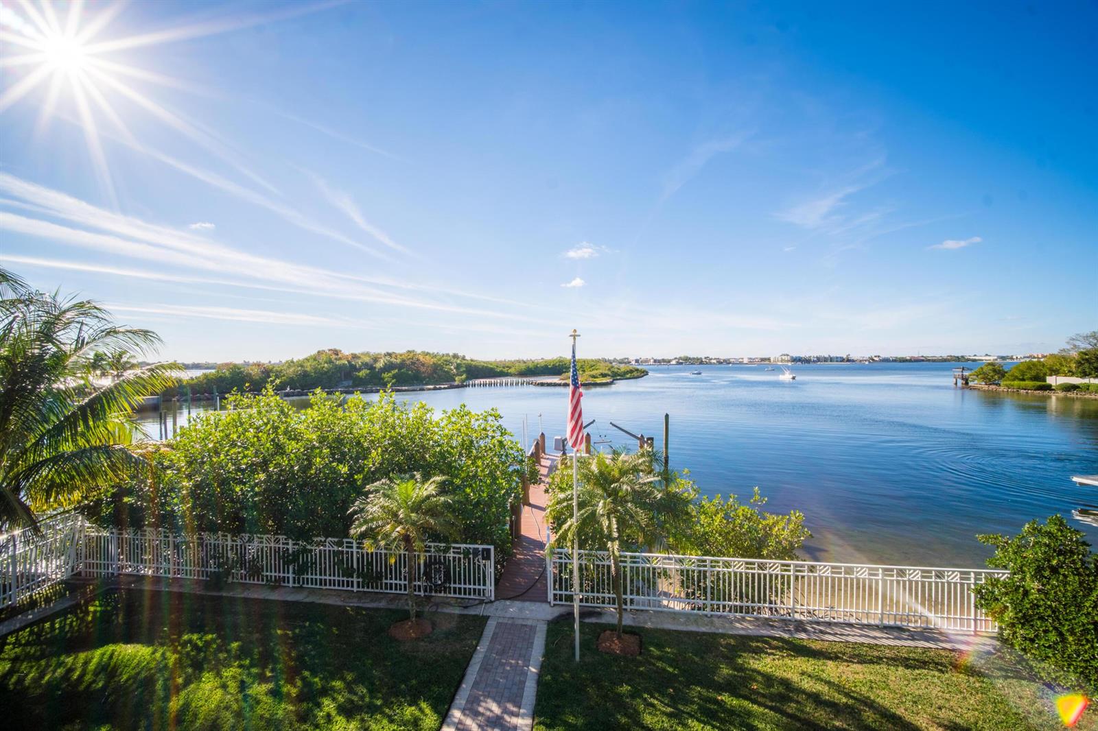 A backyard with a brick walkway, white fence, and dock overlooking a calm bay — 4000 S Ocean Boulevard, Lantana FL 33462, LANTANA, FL