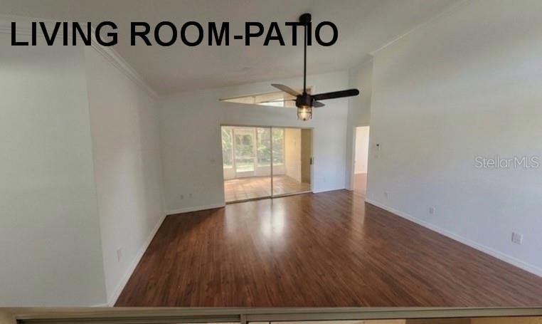 An empty living room features wood-look flooring, a vaulted ceiling with a fan, and sliding glass doors — 4613 BARNACLE DRIVE, PORT ORANGE, FL