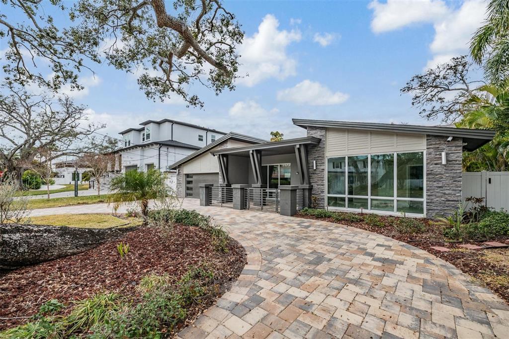 A modern single-story house with a stone facade, large windows, and a paved driveway — 4909 W DRYAD STREET, TAMPA, FL